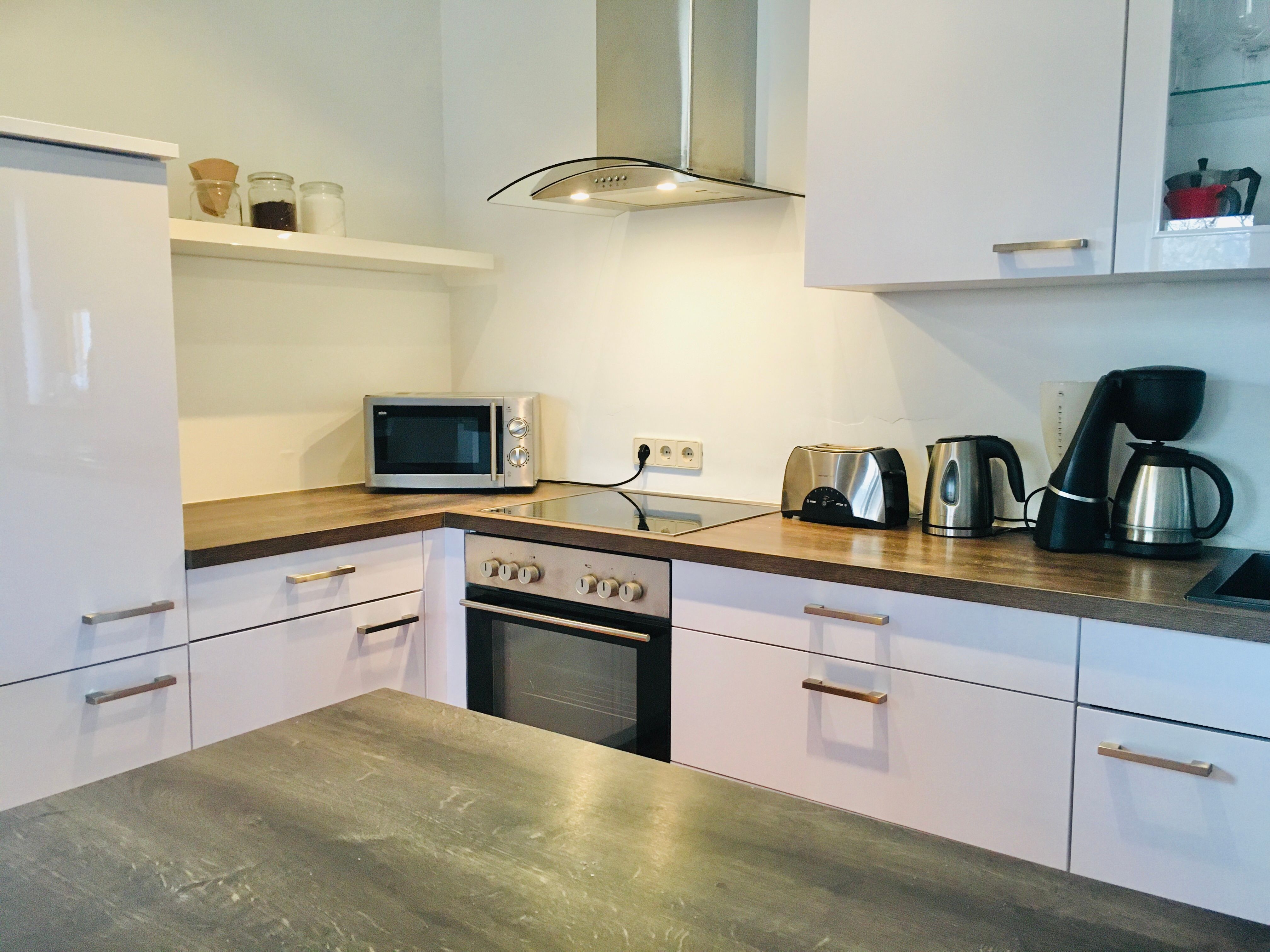 Modern kitchen with white cupboards, stove, microwave, toaster, kettle and coffee machine.