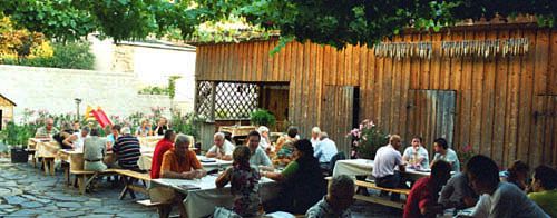 People sit at wooden tables in a cozy courtyard with vines.