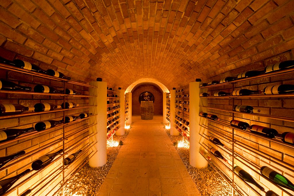 An illuminated wine cellar with brick vaults and wine bottles on shelves on the walls.