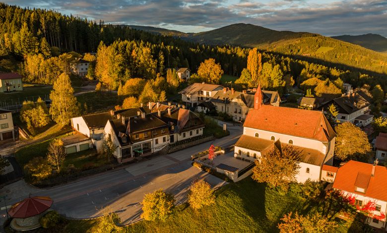 Aerial view of St. Corona am Wechsel with church and surrounding buildings in an autumnal landscape.