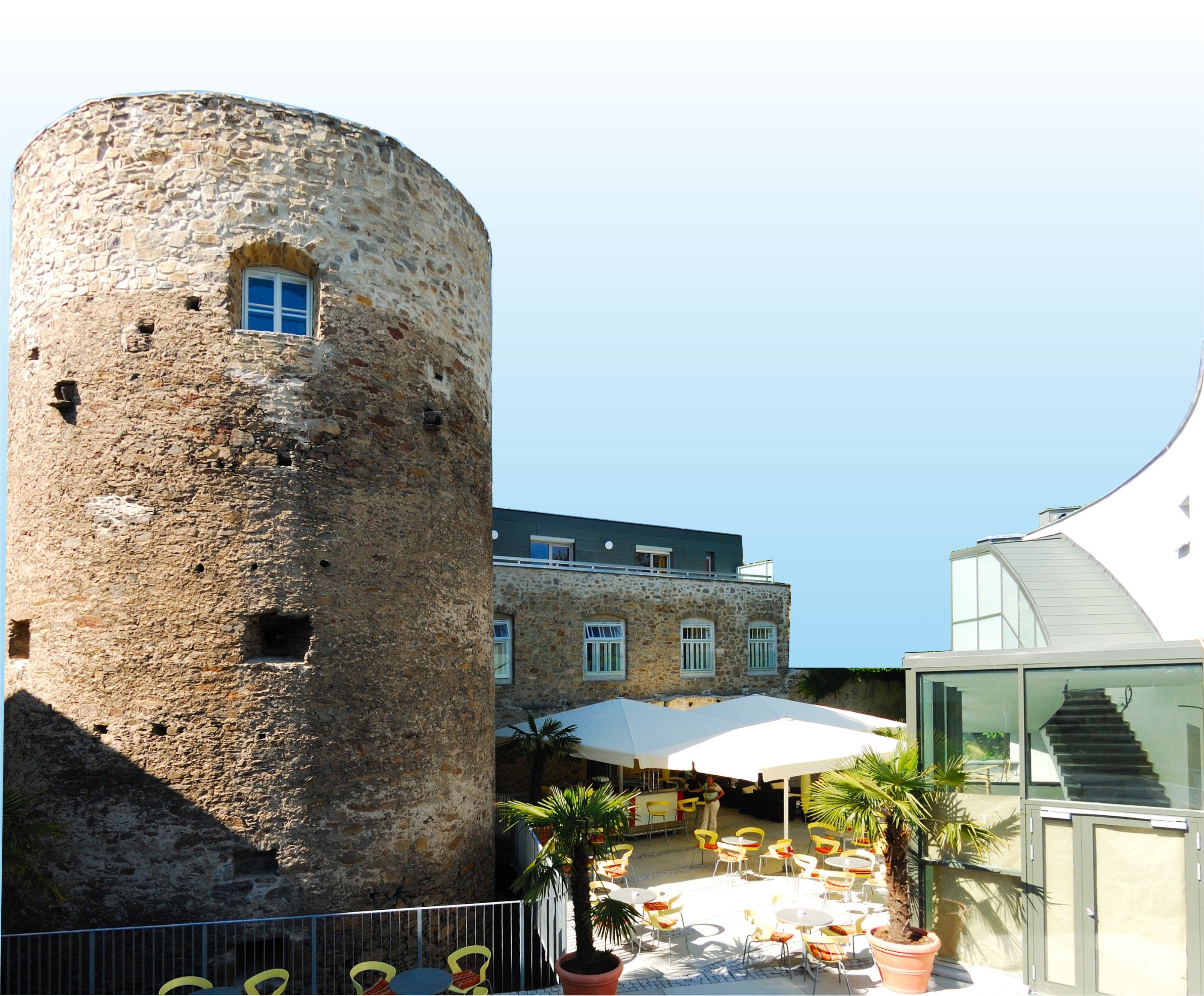 Historic tower next to modern building with terrace and parasols.