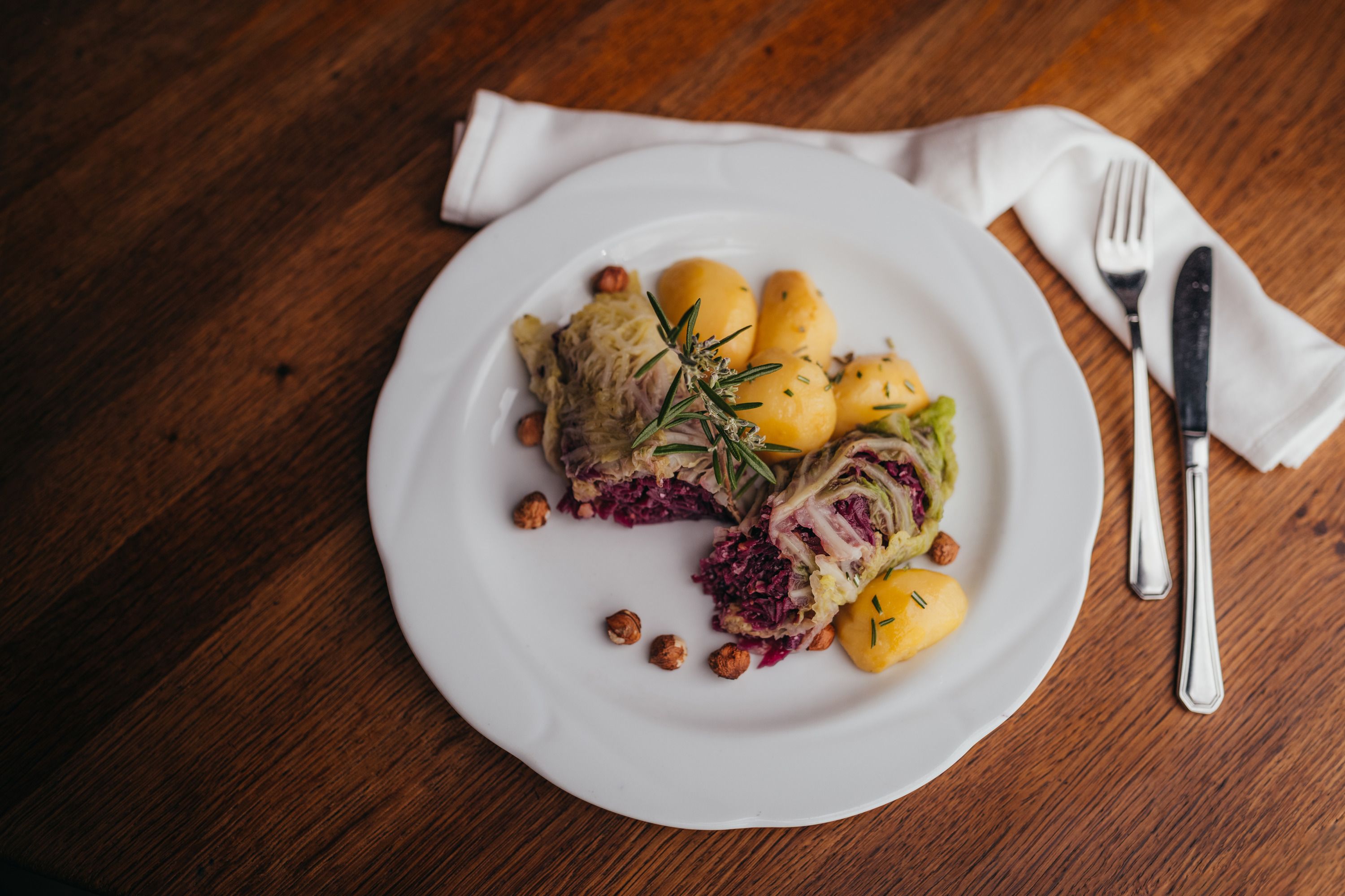 A plate of stuffed cabbage leaves, potatoes and nuts, garnished with rosemary.