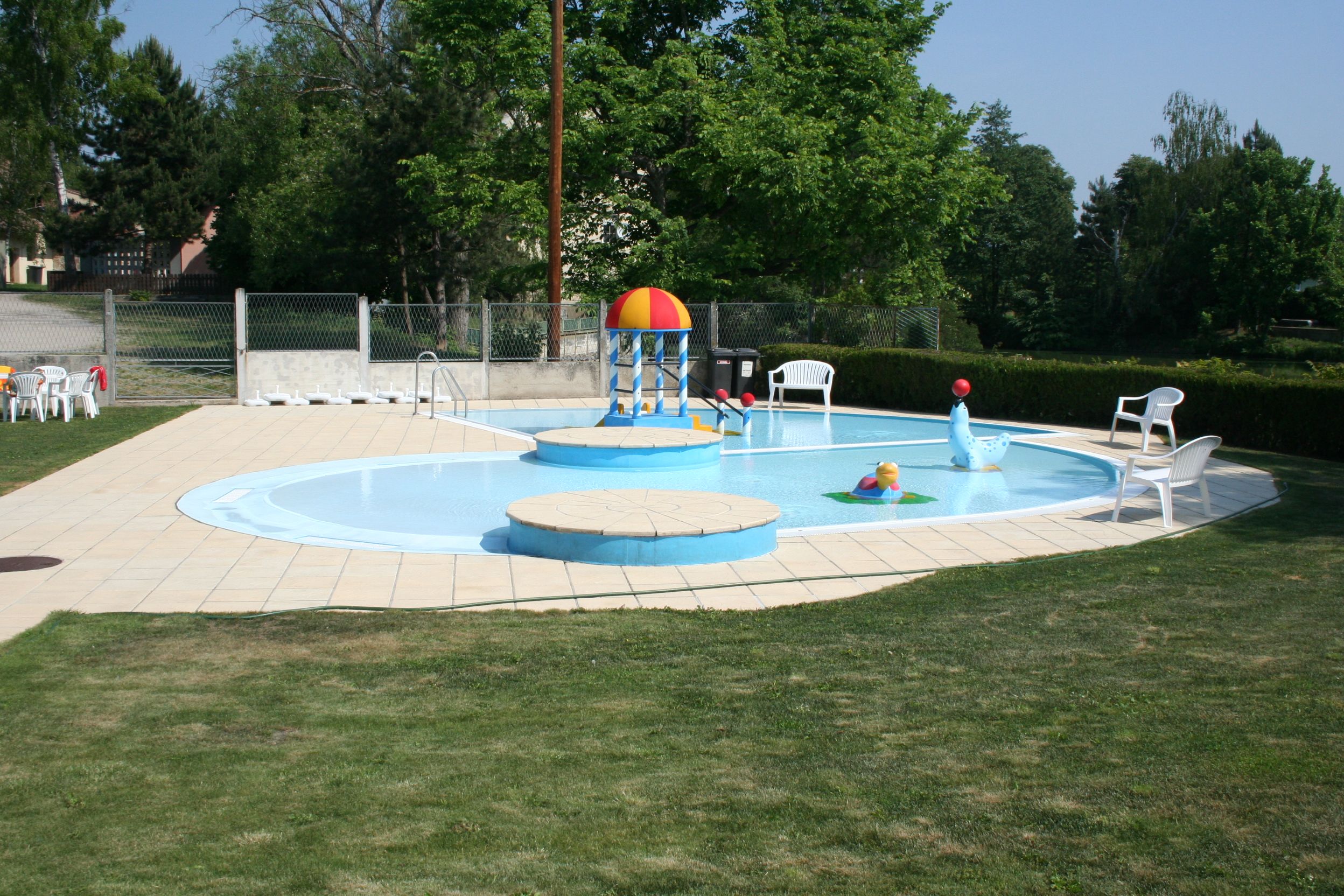 A children's paddling pool with colorful water toys and white plastic chairs on a lawn.