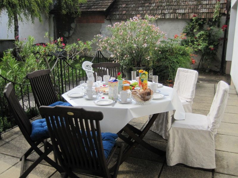 A laid table on a terrace with chairs, surrounded by plants.