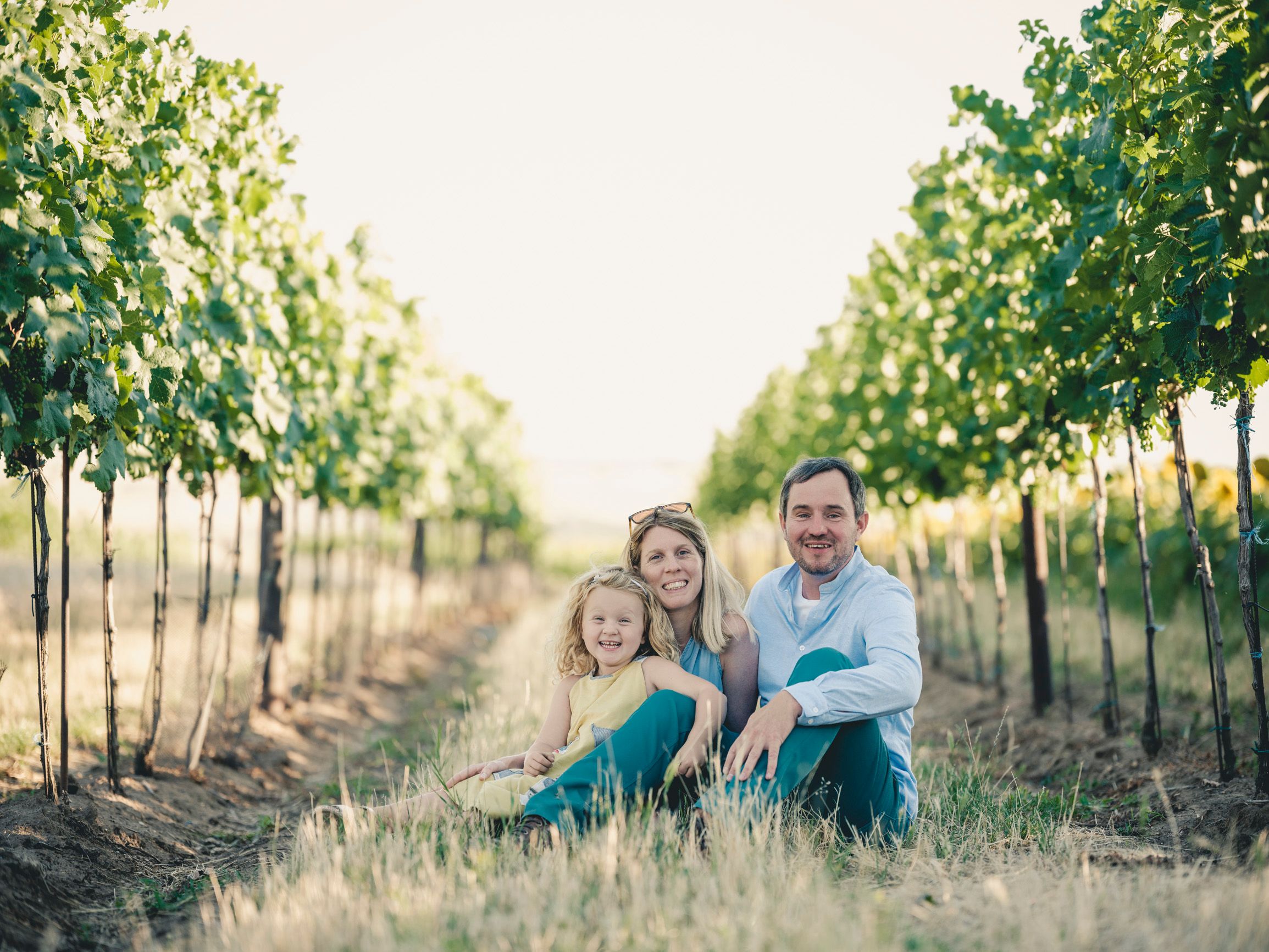 Family sitting among grapevines in a vineyard.
