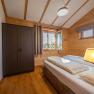 Interior view of a bedroom in a chalet with wooden walls, a double bed, a closet and a window with a view outside.