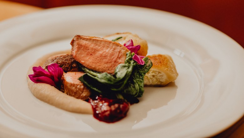 A plate of pink roast duck, cream tartlets, chestnut purée and green leaves, garnished with edible flowers.