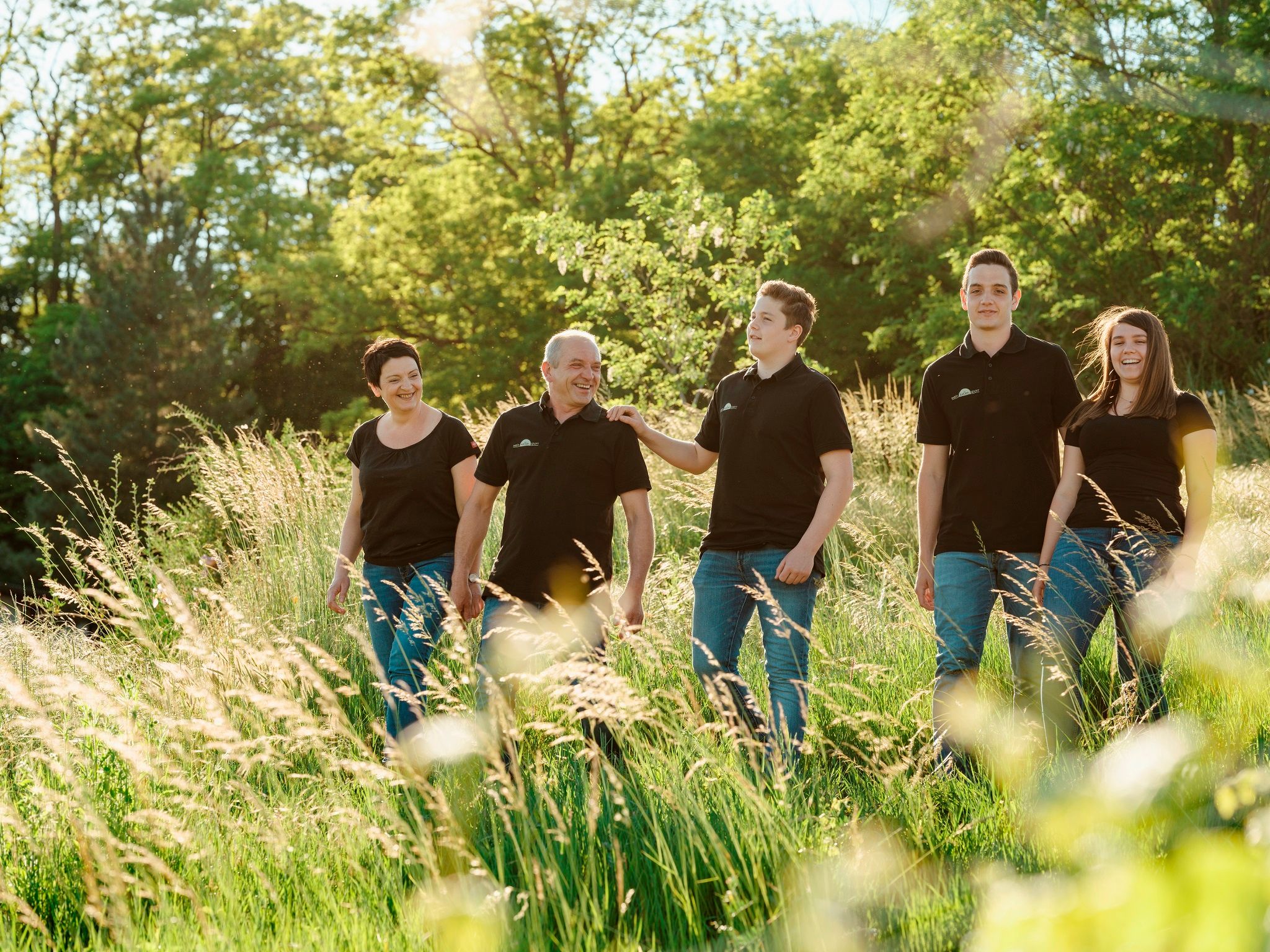 A smiling family strolls through a green meadow in the sunshine.