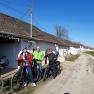 Three people with bicycles in front of a row of wine cellars in a rural setting.