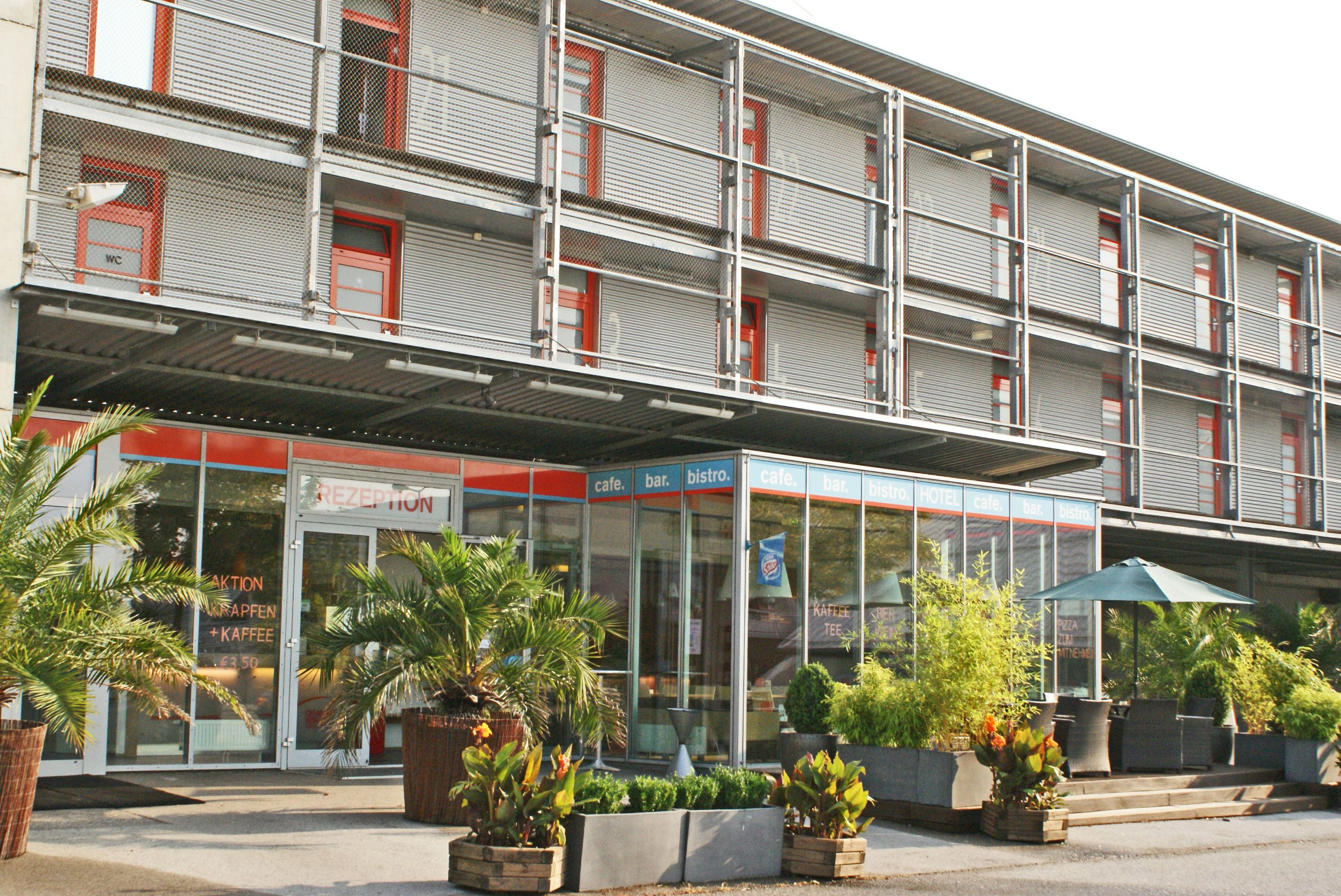 Modern hotel façade with glass front and plants.