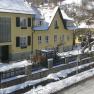 Yellow house covered with snow in winter, surrounded by a fence and trees.