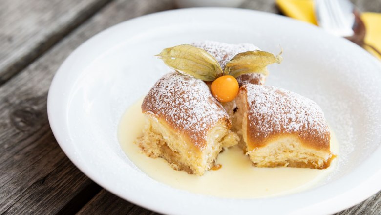 Three Buchteln with powdered sugar and physalis on vanilla sauce on a white plate.