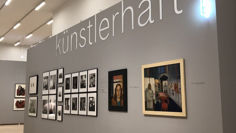 Exhibition wall with works of art and the lettering 'k&uuml;nstlerhaft'.