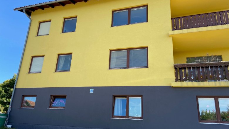 Anke's vacation apartment, © Wiener Alpen Yellow building with brown windows and balconies, blue sky in the background.