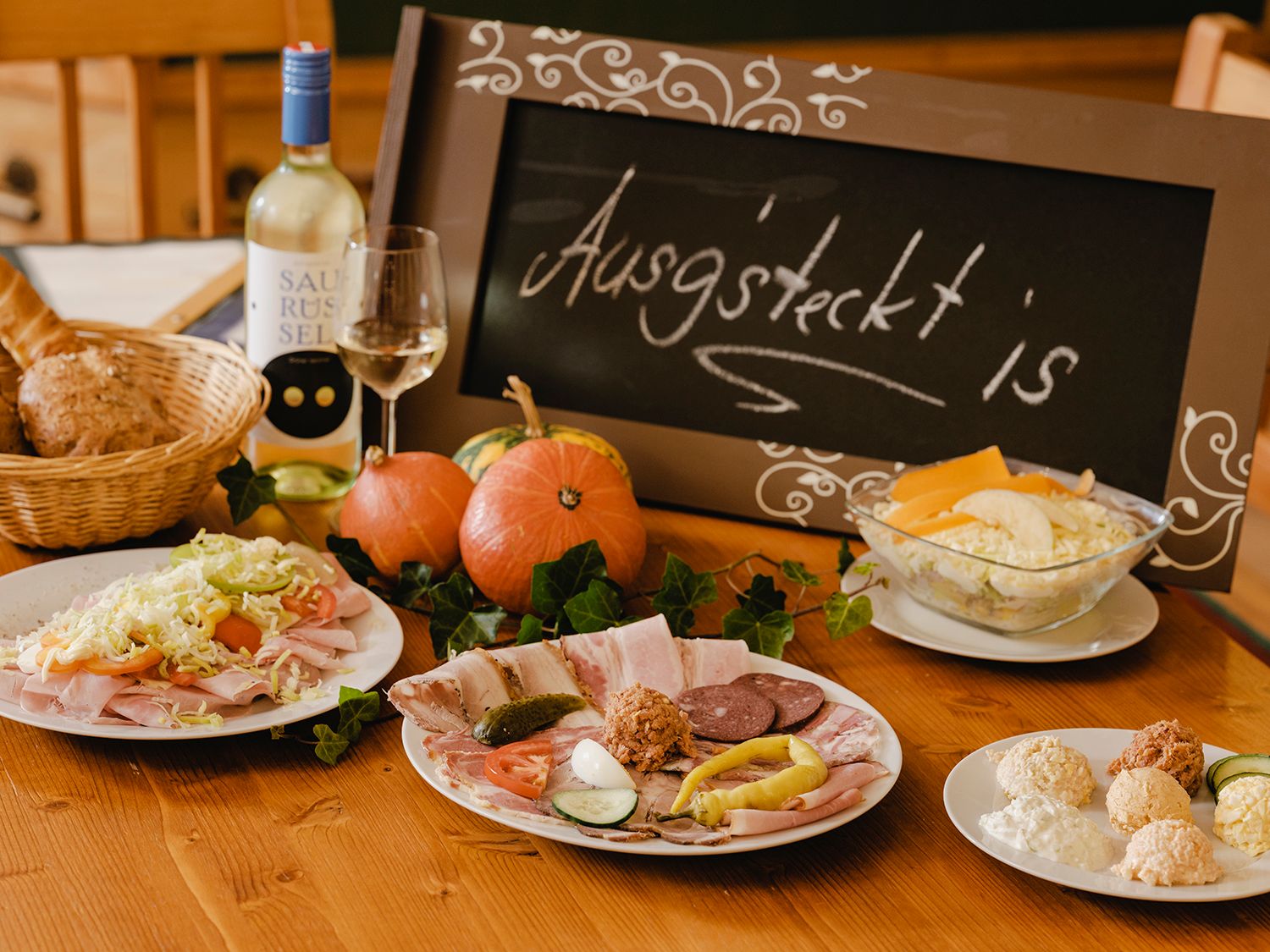 A laid table with cold plates, bread, wine and a sign saying 'Ausg'steckt is'.