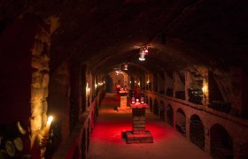 An atmospherically lit wine cellar with bottles on stone pillars.