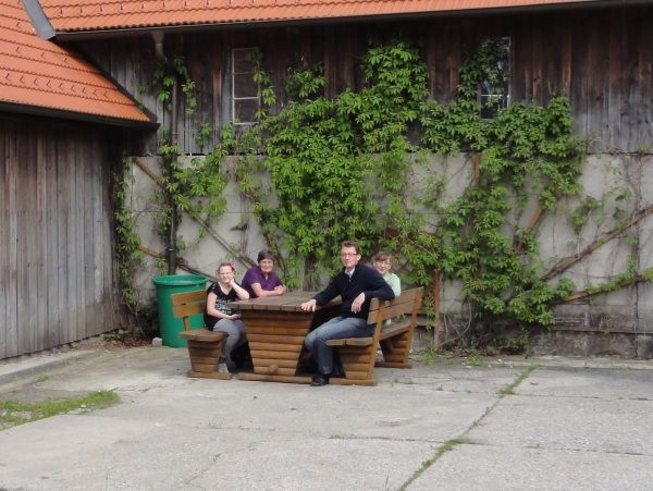 Four people sit at a wooden table in front of a building overgrown with ivy.