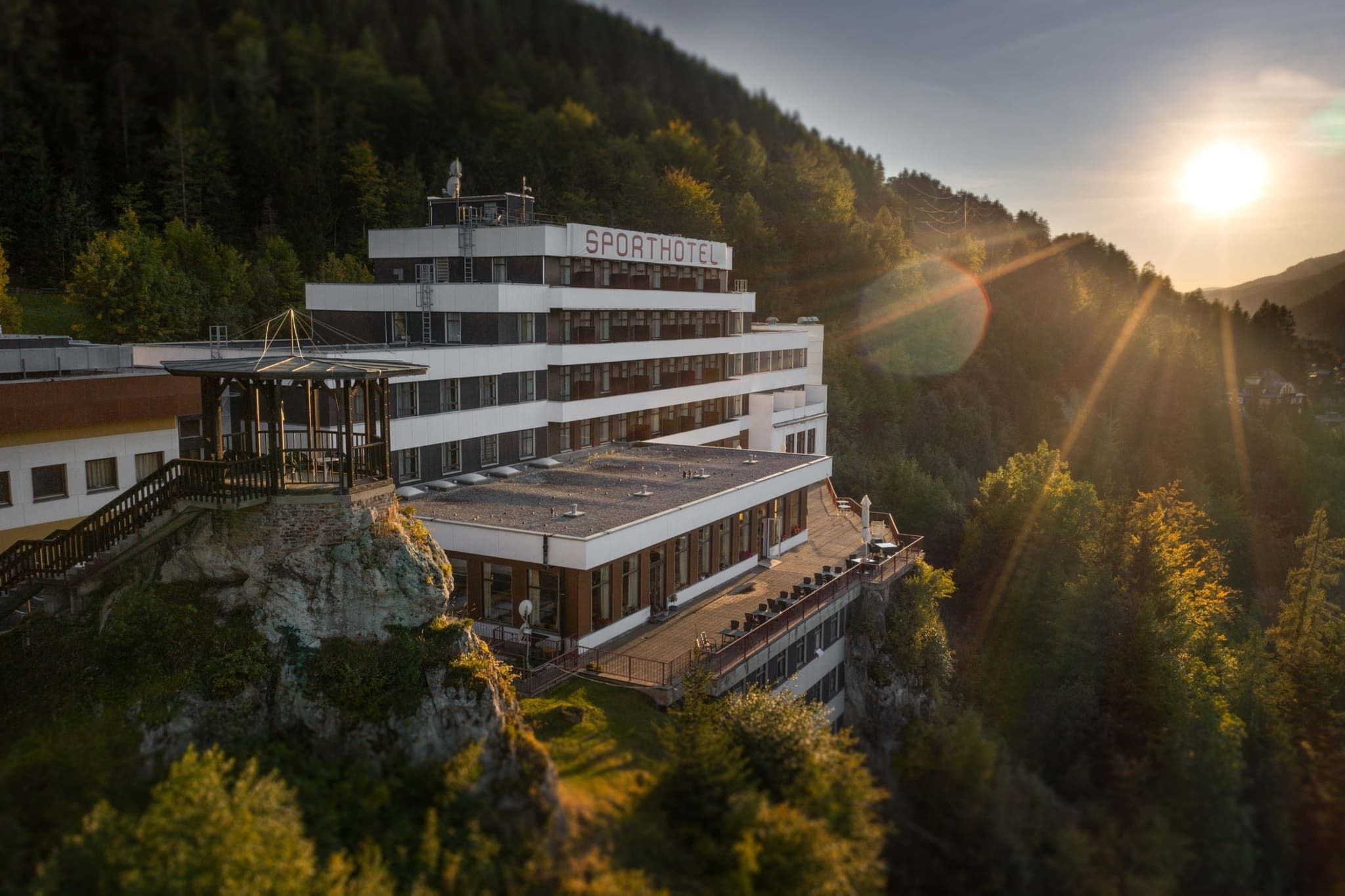 A hotel on a hill at sunset, surrounded by forest.