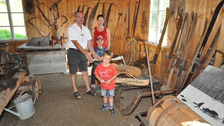 A family in a rustic room with old farming tools and equipment.