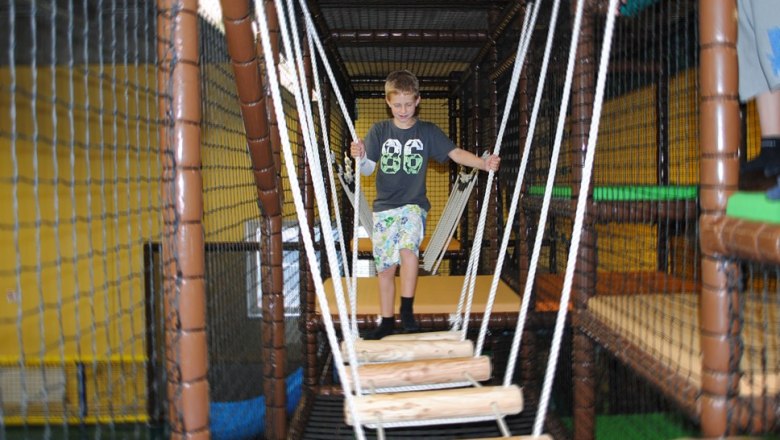 A boy balances on a suspension bridge in an indoor climbing garden.