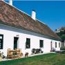 White farmhouse with red tiled roof and garden furniture, in the background a castle on a hill.