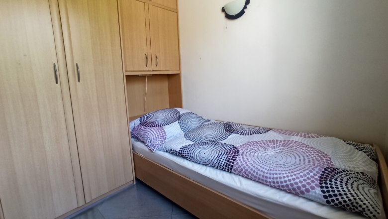 A simple bedroom with a single bed and a large wooden wardrobe.
