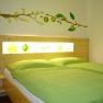 A cozy room with a double bed, green bed linen and a wall decoration with yellow flowers and fruits.