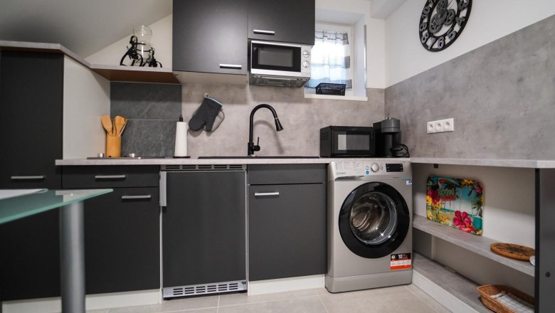 Modern kitchen with black cupboards, washing machine, microwave and coffee machine.