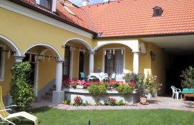 Yellow house with red roof, arcades and terrace with flowers.
