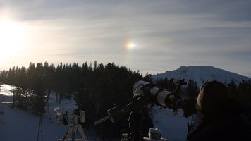 Telescopes on a snowy summit station with a solar halo in the background.