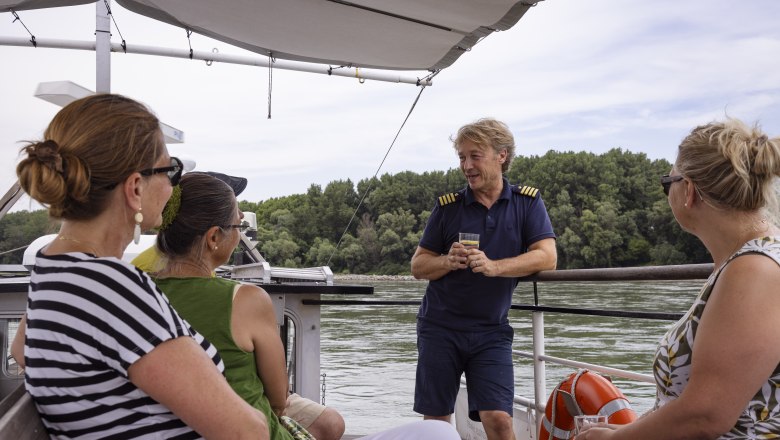 People on a boat on the Danube, a man in uniform (captain) talks to three women.