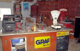 A historic village store with an old cash register, scales and various products on a counter.