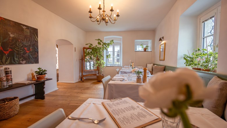 Cozy restaurant with wooden floor, white tablecloths and plants.