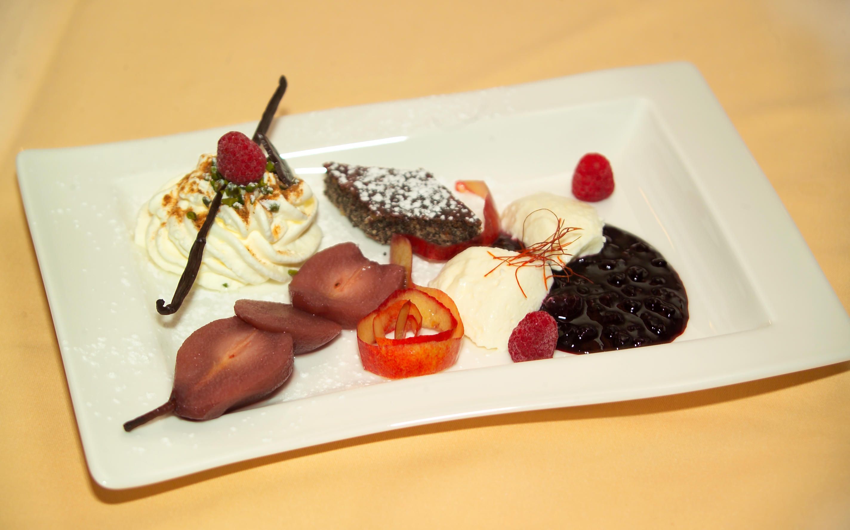A dessert plate with various desserts, including cream, berries, chocolate cake and poached pears.