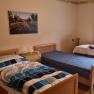 A simply furnished bedroom with two single beds, a table and chair and a window with curtains.