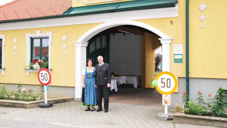 A couple is standing in front of a yellow building with the sign 'Weinbau Haller'.