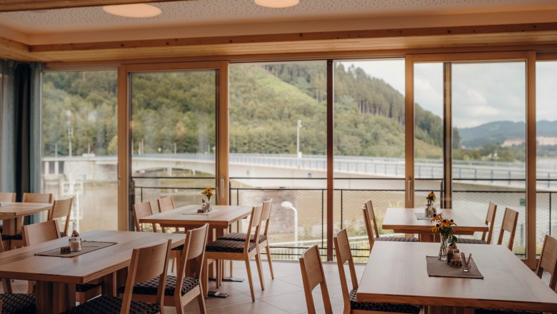 Interior view of an inn with large windows and a view of a bridge and wooded hills.