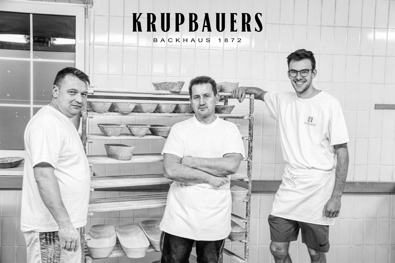 Three bakers in a bakery with bread baskets in the background.