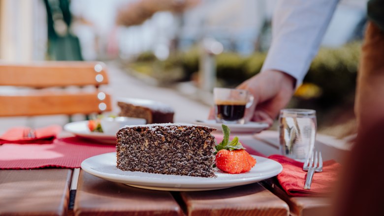 Poppy seed cake with strawberry and espresso served on a wooden table outside.