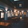 Illuminated courtyard with wooden benches and tables, surrounded by a building with arched windows.
