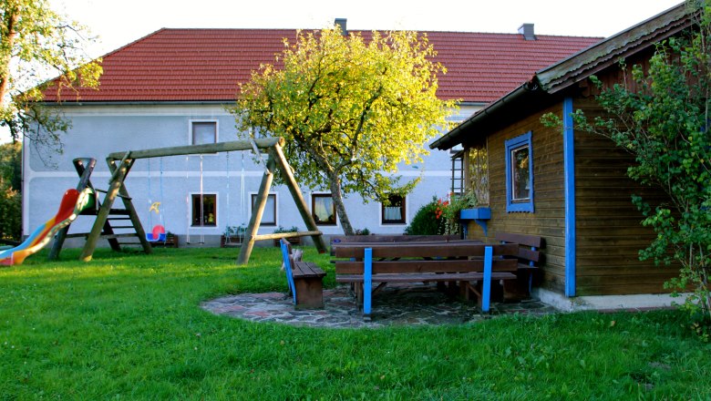 Pichelbauer, © Fam. Wiesinger A playground with a swing, slide and benches in front of a house with a red roof.