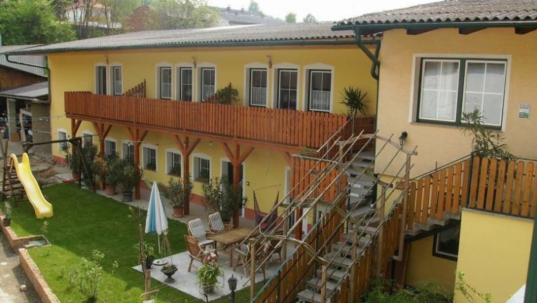 Yellow building with wooden balcony and garden with slide and seating area.