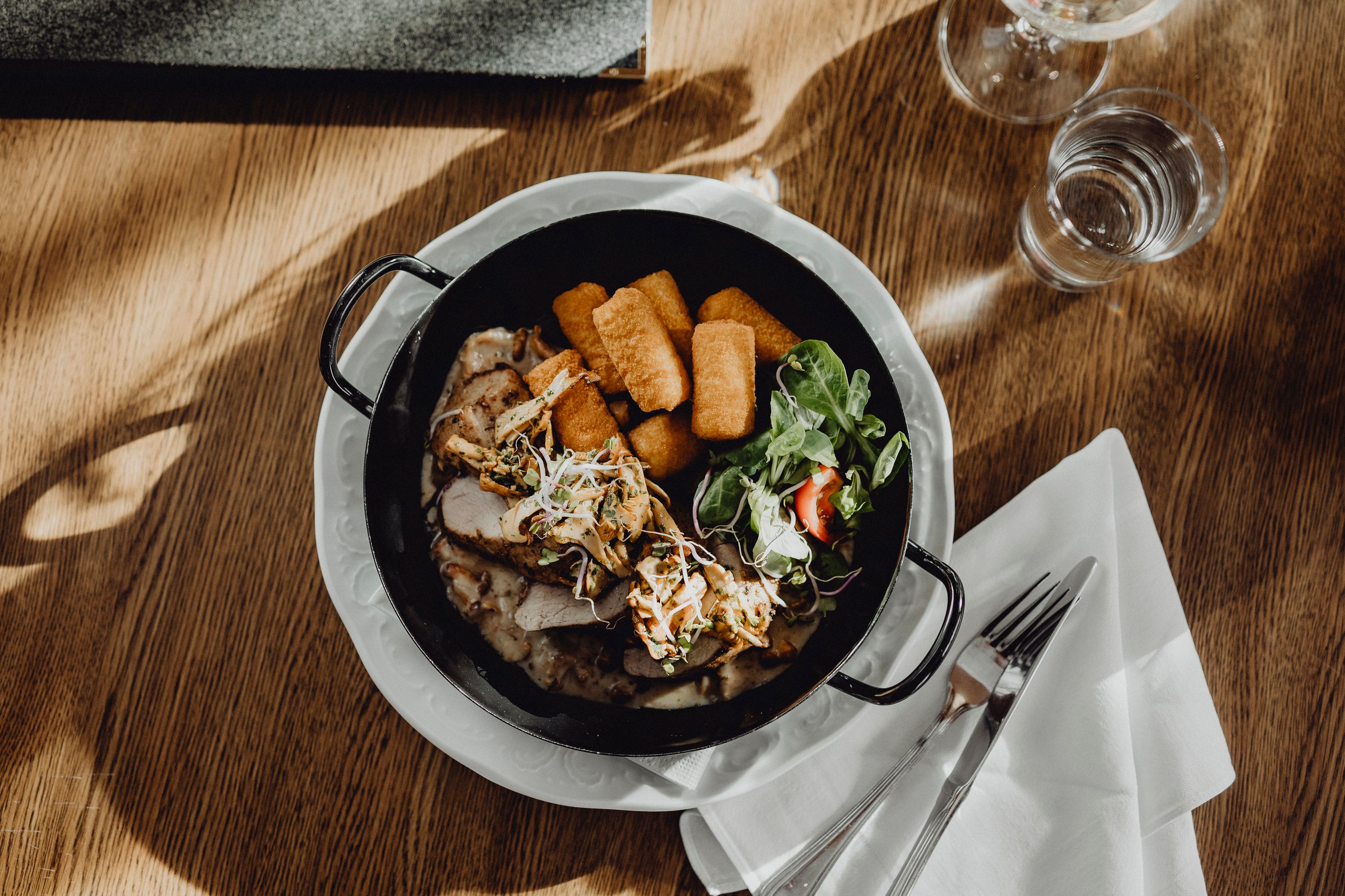 A plate of pork fillet, chanterelles, croquettes and salad on a wooden table.