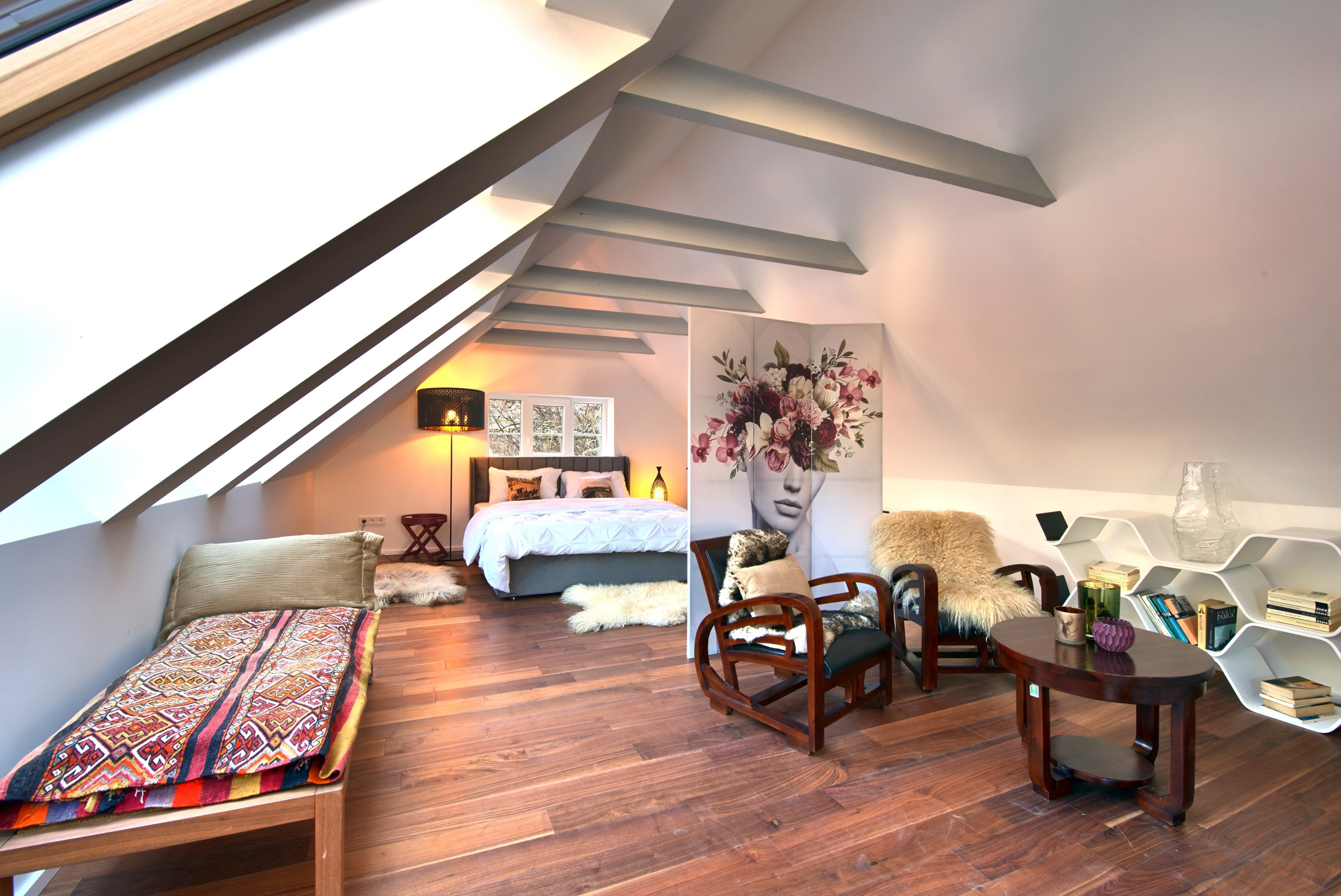 Modern bedroom in the attic with wooden floor, bed, armchairs and decorative room divider.