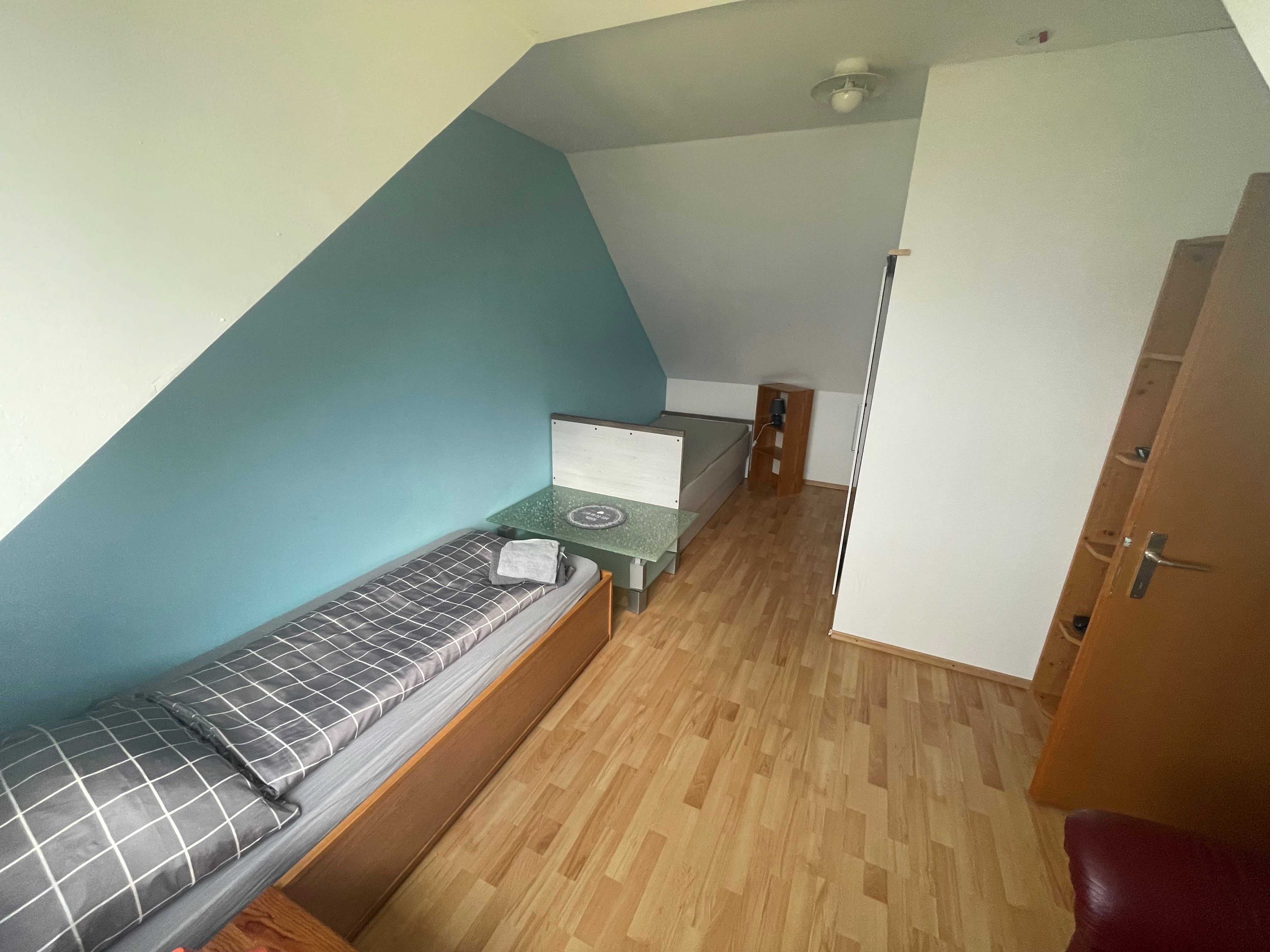 A room with a single bed, a small table and a shelf. The walls are painted blue and white.