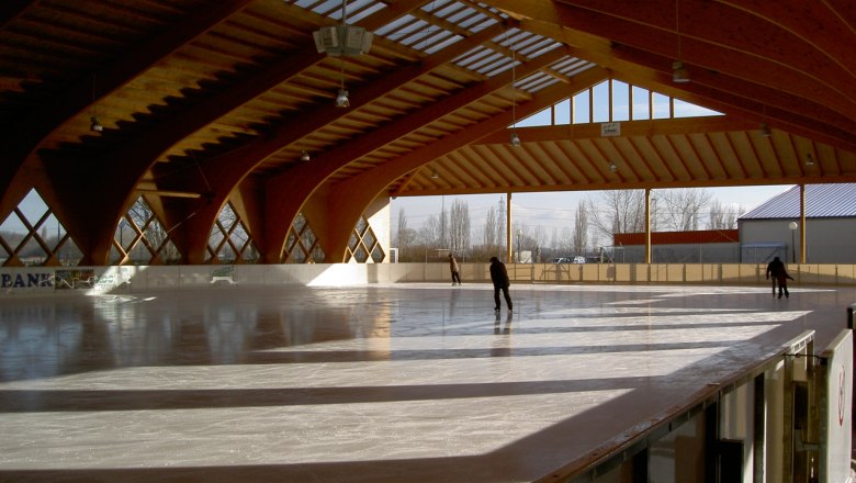 Covered artificial ice rink with wooden structure and skaters.