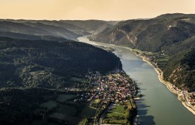 Aerial view of Aggsbach Markt an der Donau, surrounded by hills and forests.