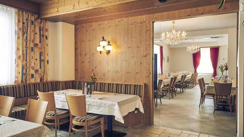 A cozy guest room with wooden walls and an adjoining ballroom with chandeliers and laid tables.