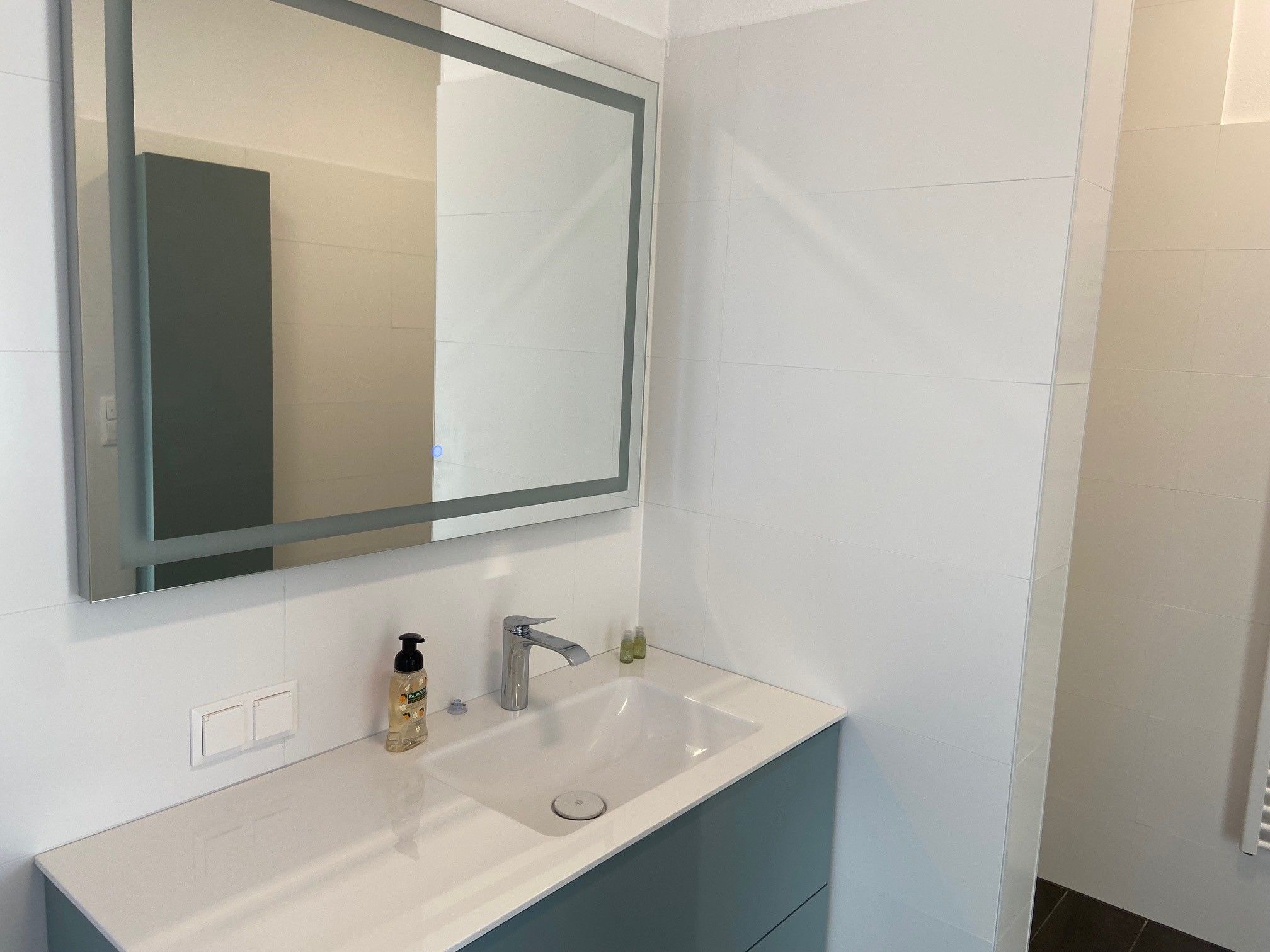 Modern bathroom with mirror, washbasin and soap dispenser.