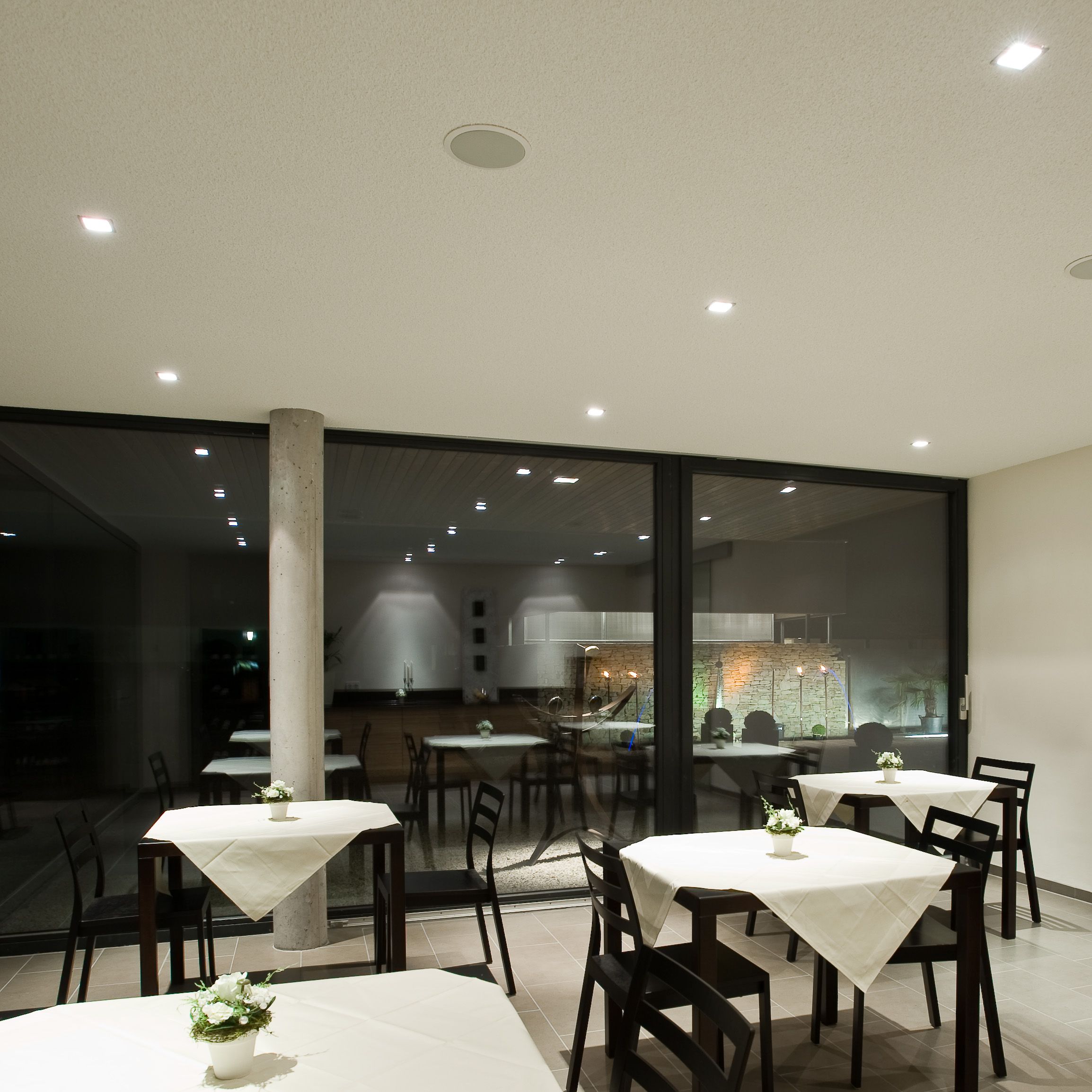 Modern breakfast room with tables and chairs, decorated with white tablecloths and flowers.